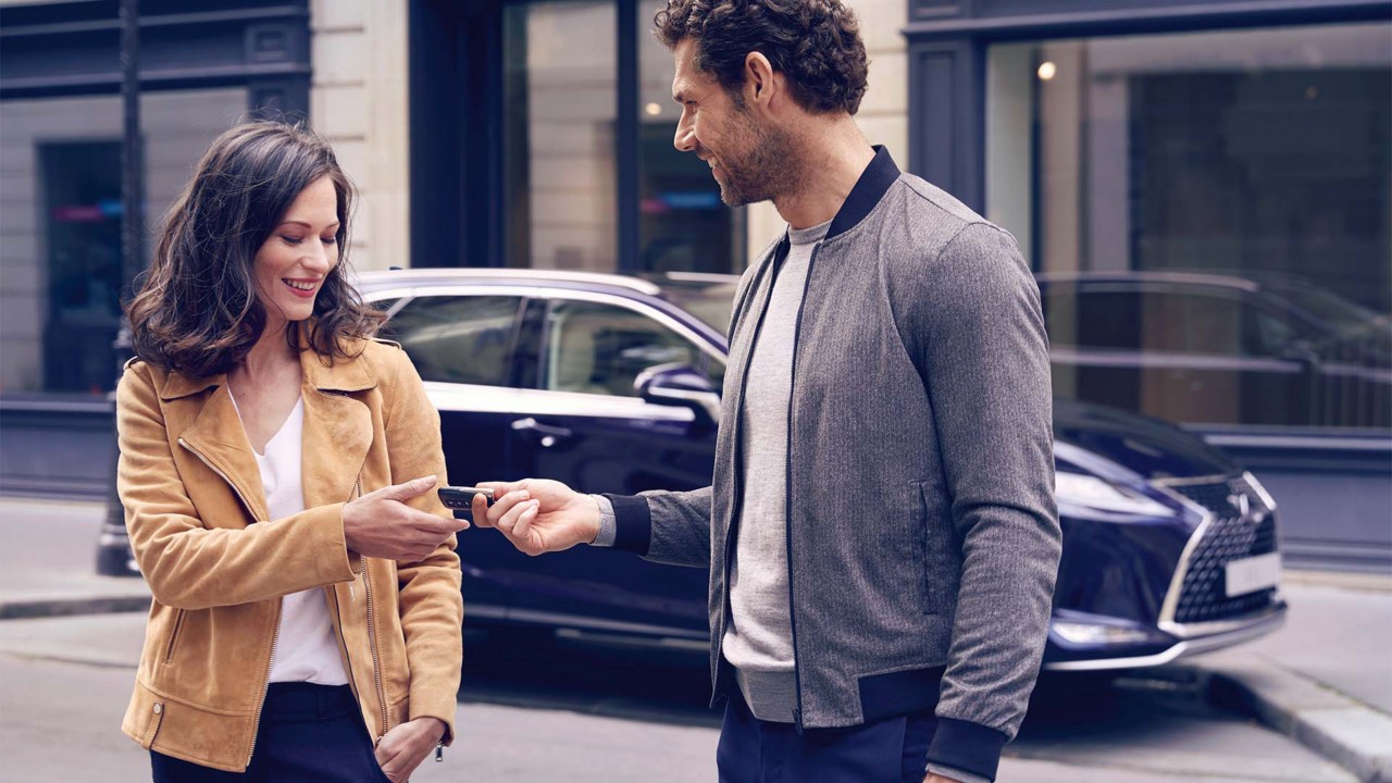 A man handing over a Lexus key to a woman