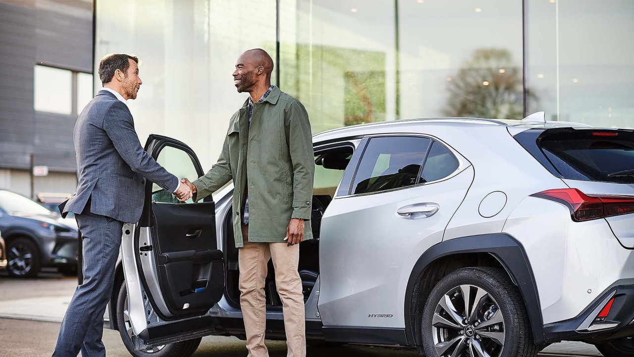 Two men shaking hands in front of a Lexus 